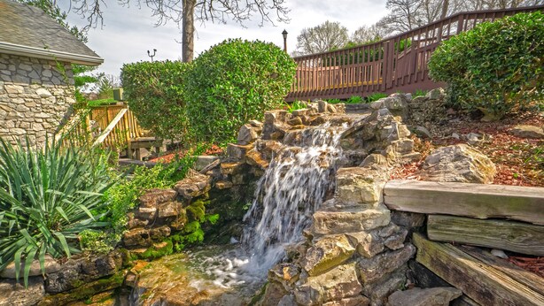 A small waterfall in a landscaped garden with stone walls and wooden railings.
