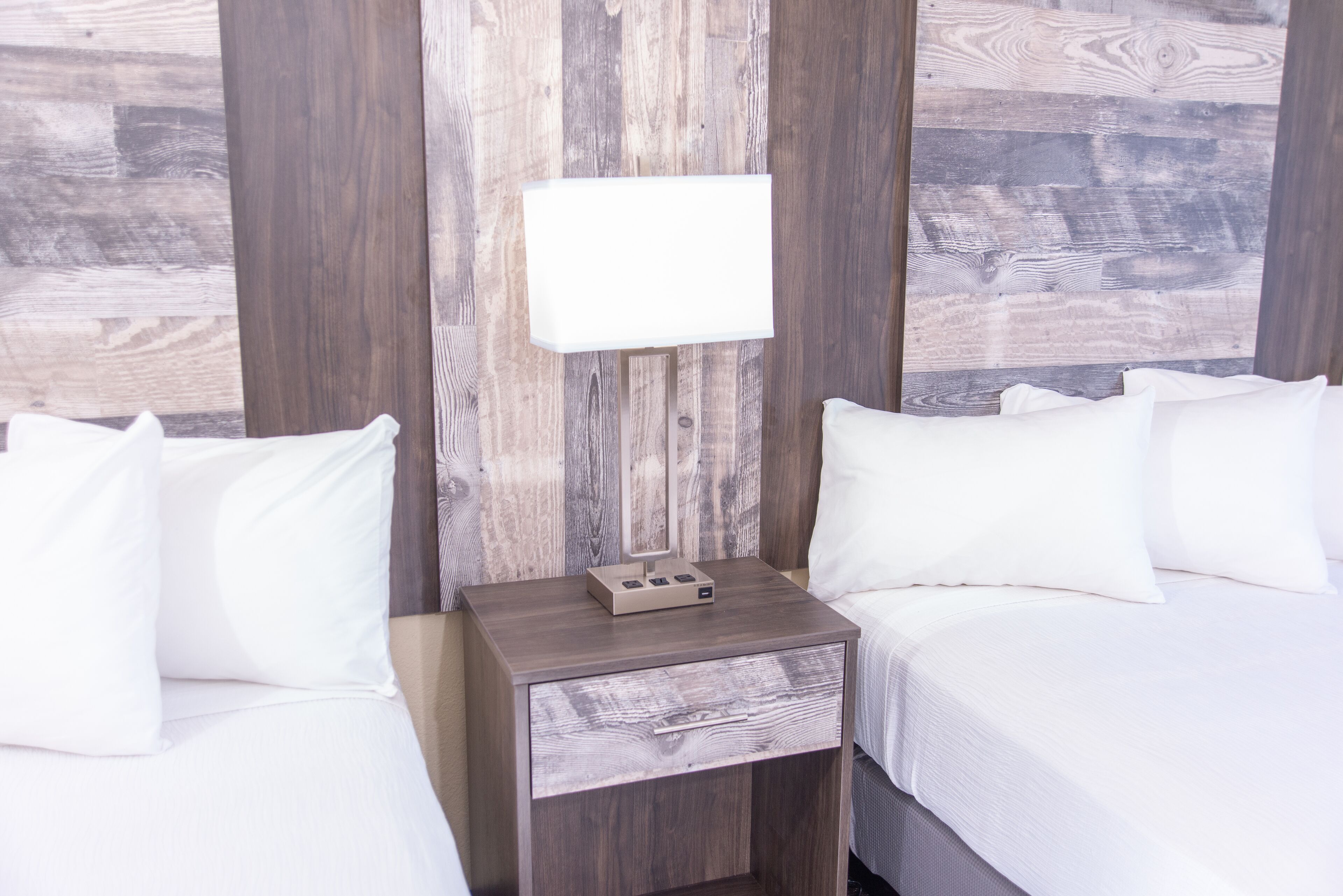 Une chambre d’hôtel avec deux lits, une table de chevet avec une lampe et un lambris en bois.