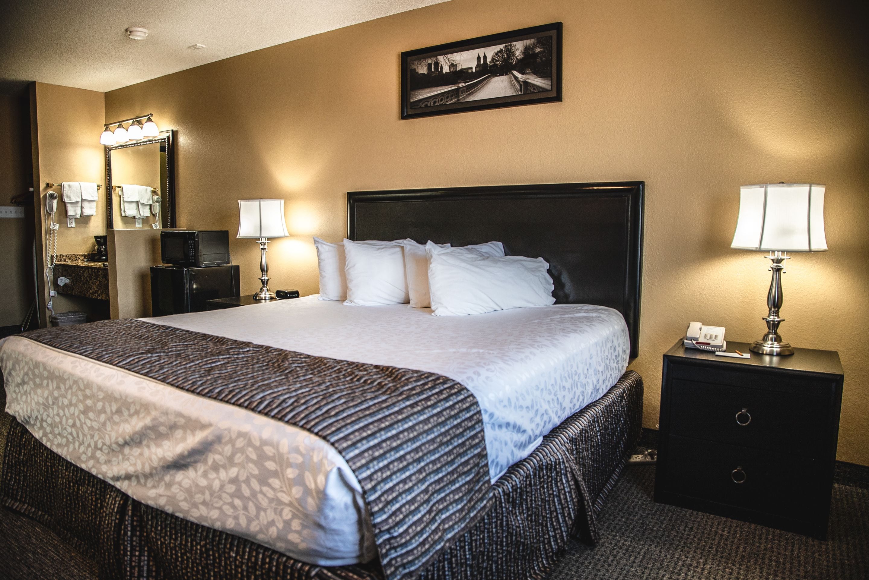 A hotel room with a large bed, a bedside table with a lamp, a mirror, and a picture on the wall.