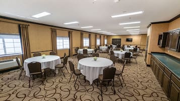 A conference room with multiple round tables and chairs, arranged in a U-shape, with a patterned carpet and large windows along one wall.