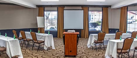 A conference room with a podium, white tables, brown chairs, and a projector screen.
