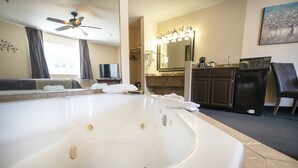 A hotel bathroom with a large bathtub, a vanity with a mirror, a ceiling fan, and a microwave on the countertop.