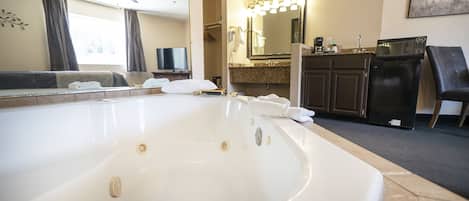 A hotel bathroom with a large bathtub, a vanity with a mirror, a ceiling fan, and a microwave on the countertop.