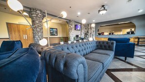 A lobby with a grey sofa, a blue armchair, and a stone pillar.