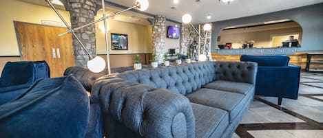 A lobby with a grey sofa, a blue armchair, and a stone pillar.