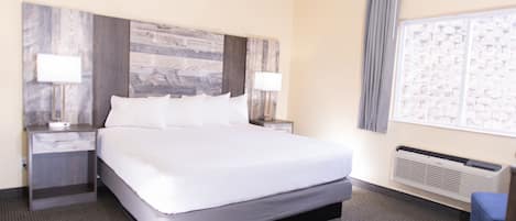 Habitación de hotel con una cama grande, dos mesitas de noche con lámparas, un ventanal con vistas y un aire acondicionado instalado.