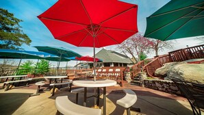 An outdoor patio with round tables and benches, surrounded by red and green umbrellas.