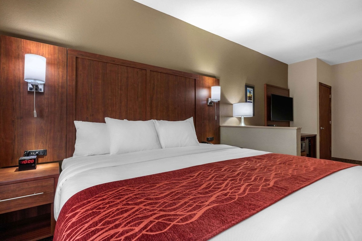 A hotel room with a large bed, wooden headboard, bedside lamps, a TV, and a clock on the nightstand.