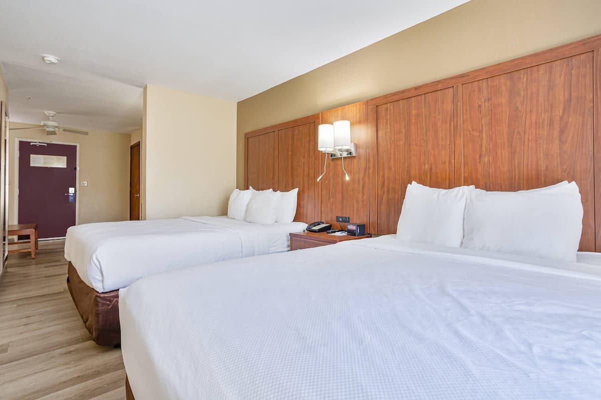 A hotel room with two beds, wooden headboard, bedside tables with lamps, and a ceiling fan.
