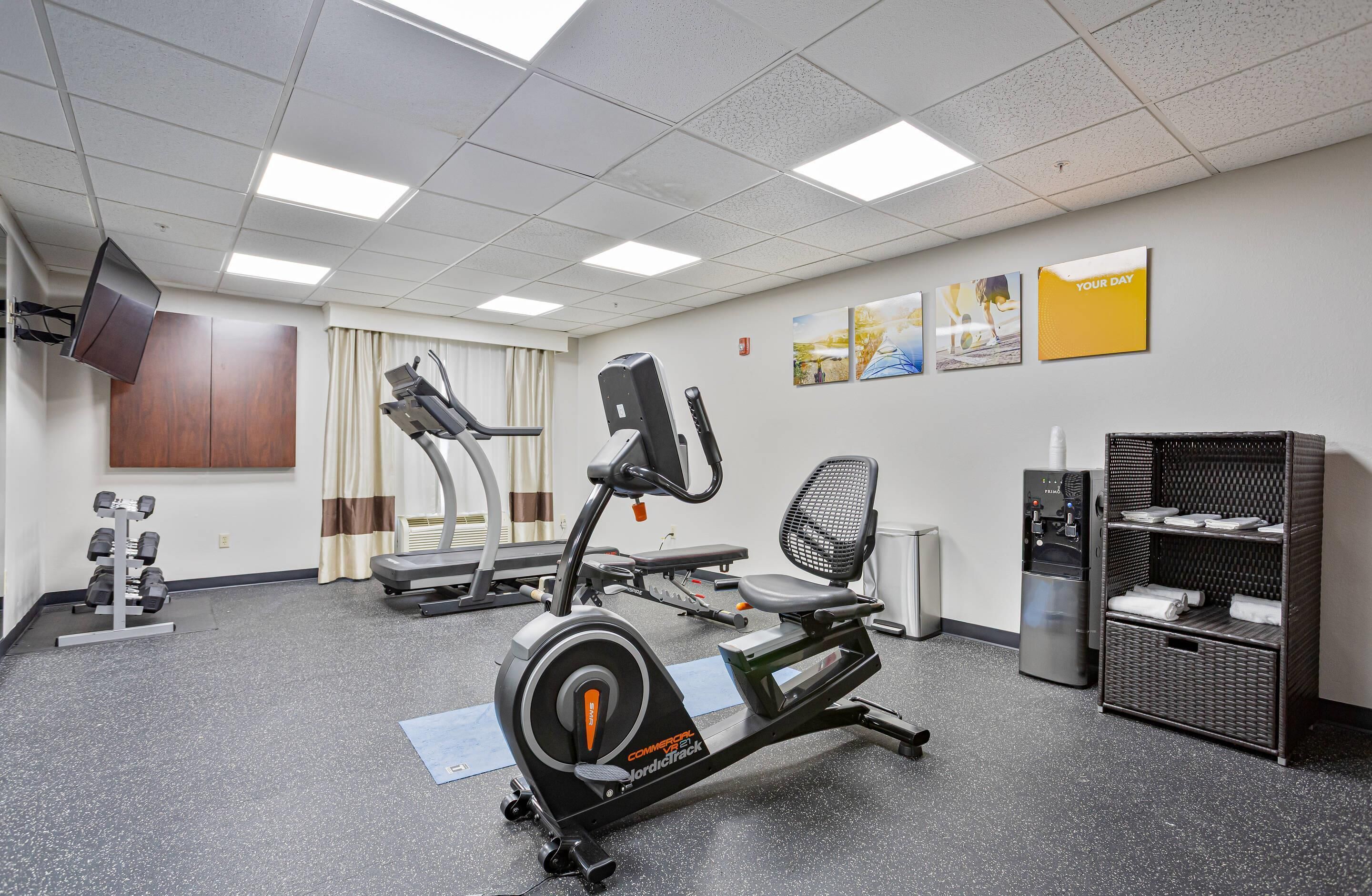 Un gimnasio con máquinas de cardio, mancuernas, un dispensador de agua y un mueble de almacenamiento de mimbre.