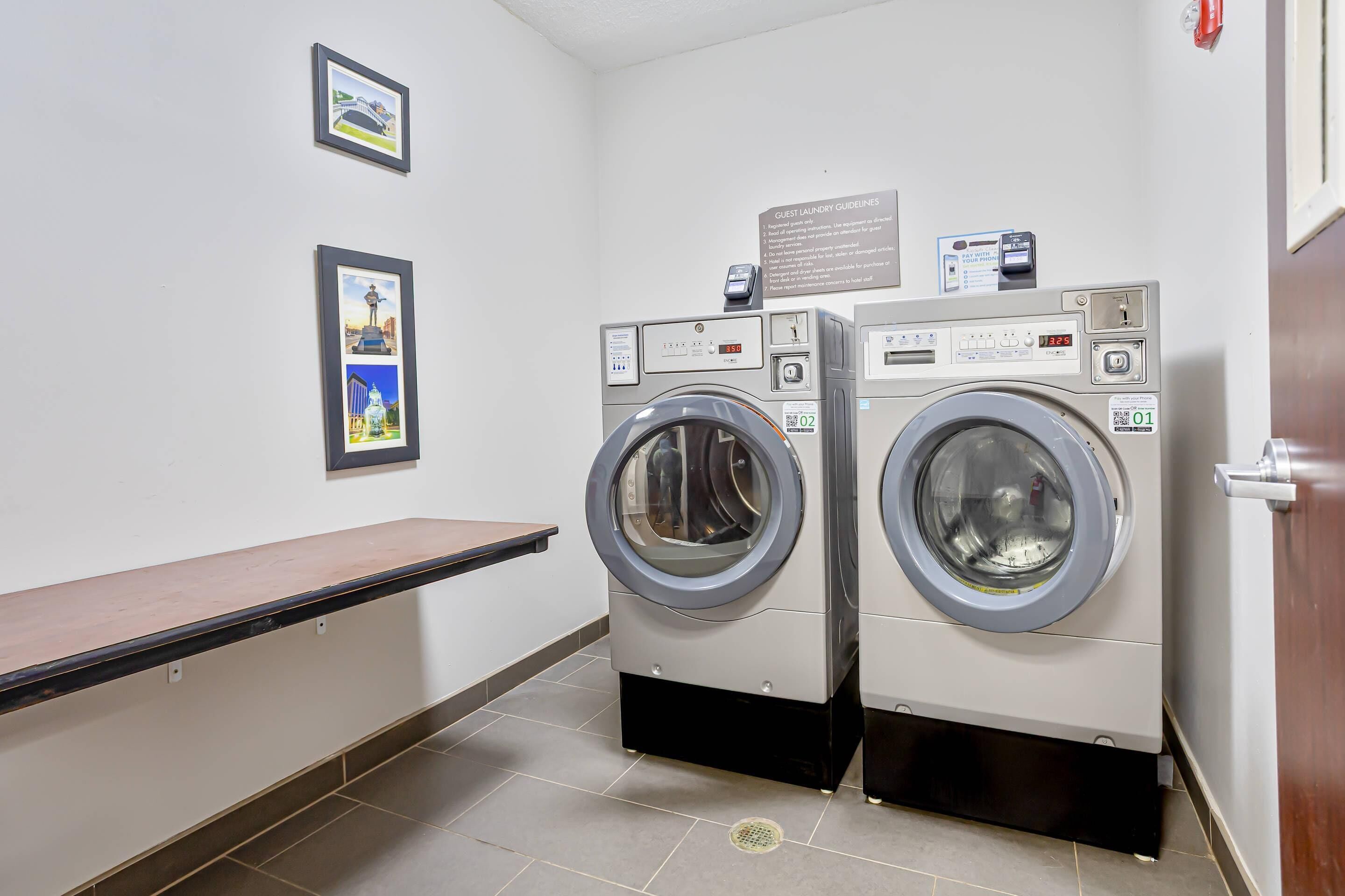 A laundry room with two front-loading washing machines, a bench, and a sign with guest laundry guidelines.