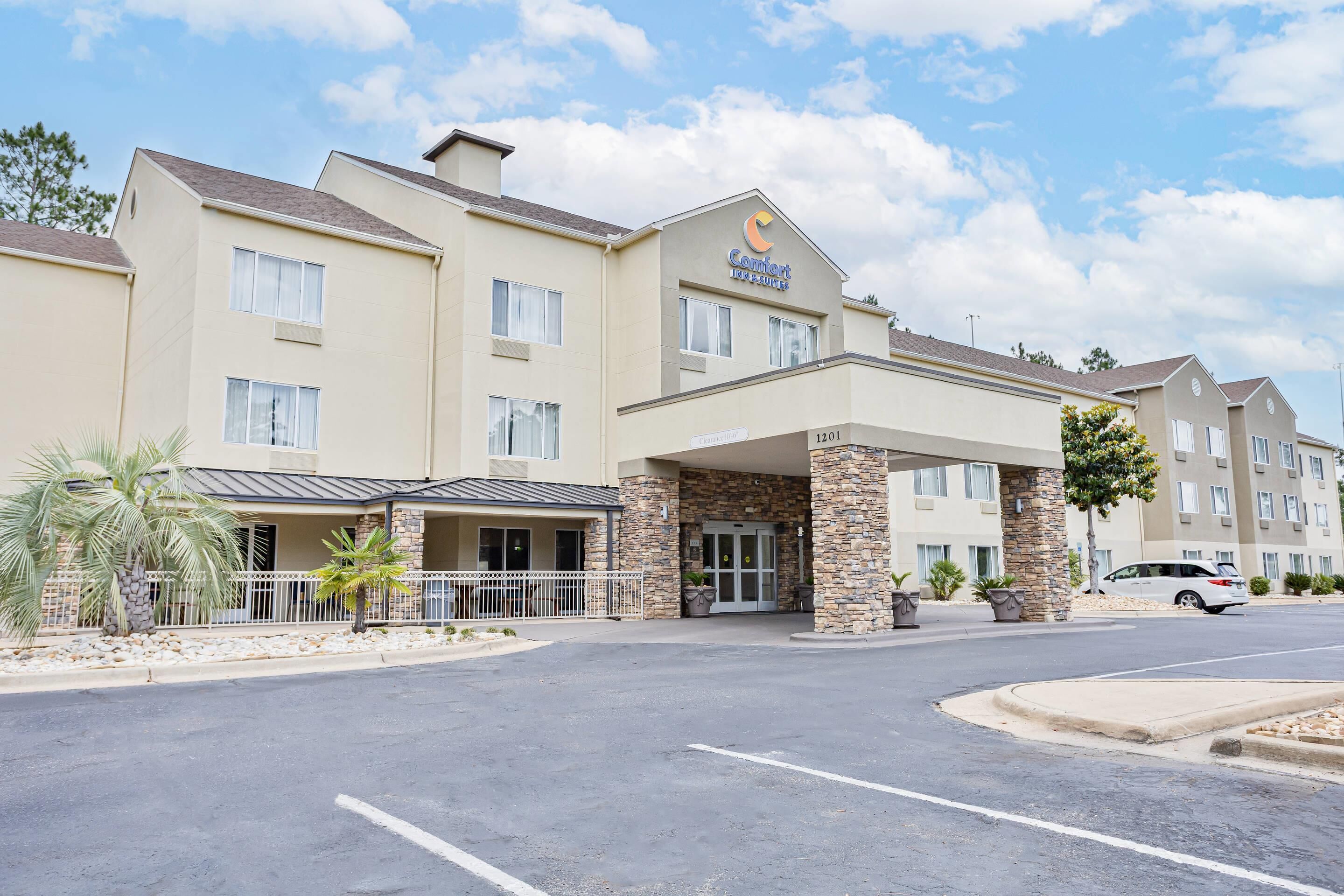 A hotel with a beige exterior, a covered entrance, and a parking lot.