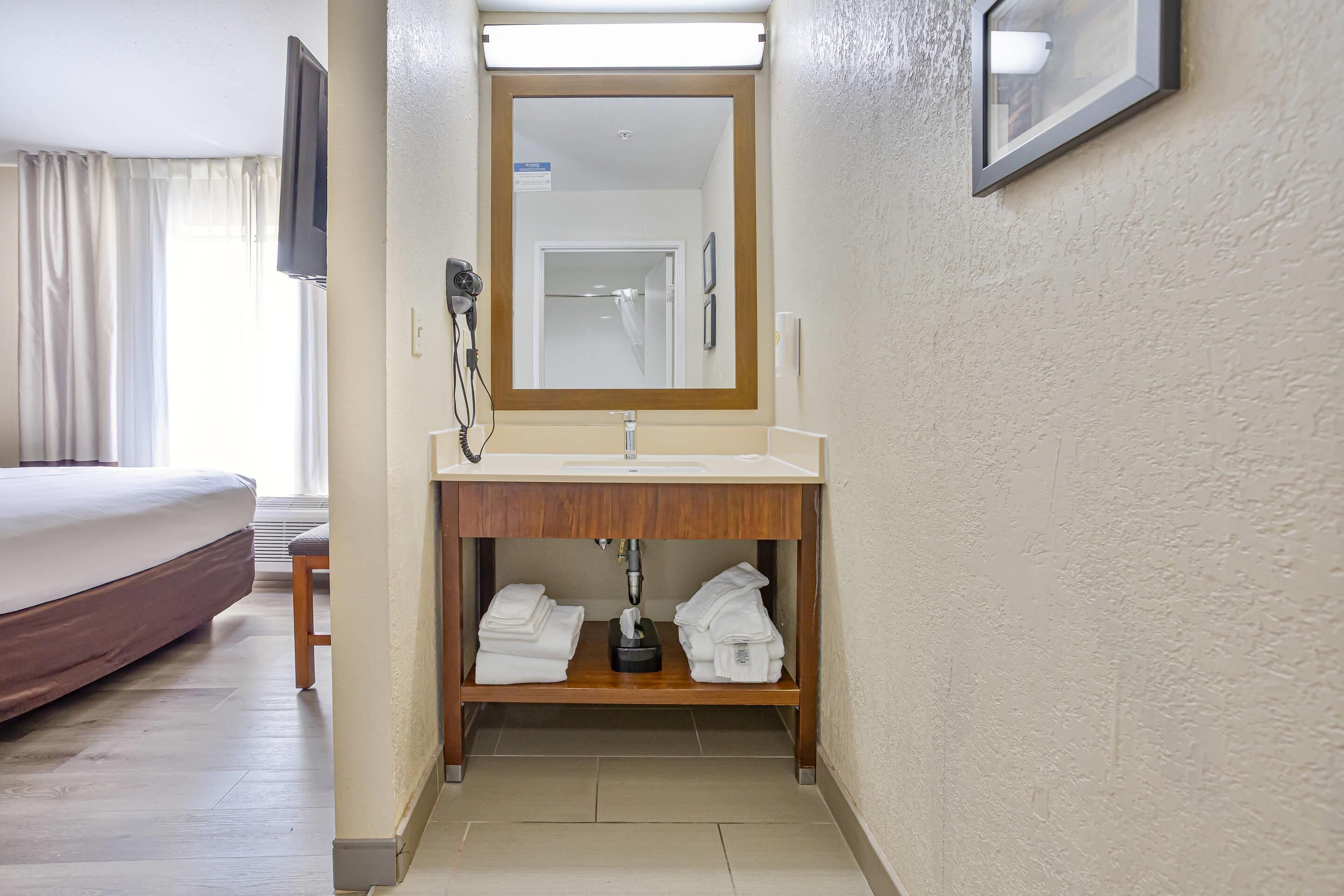 Een hotelbadkamer met een houten wastafelmeubel, een wastafel, een spiegel en een haardroger.