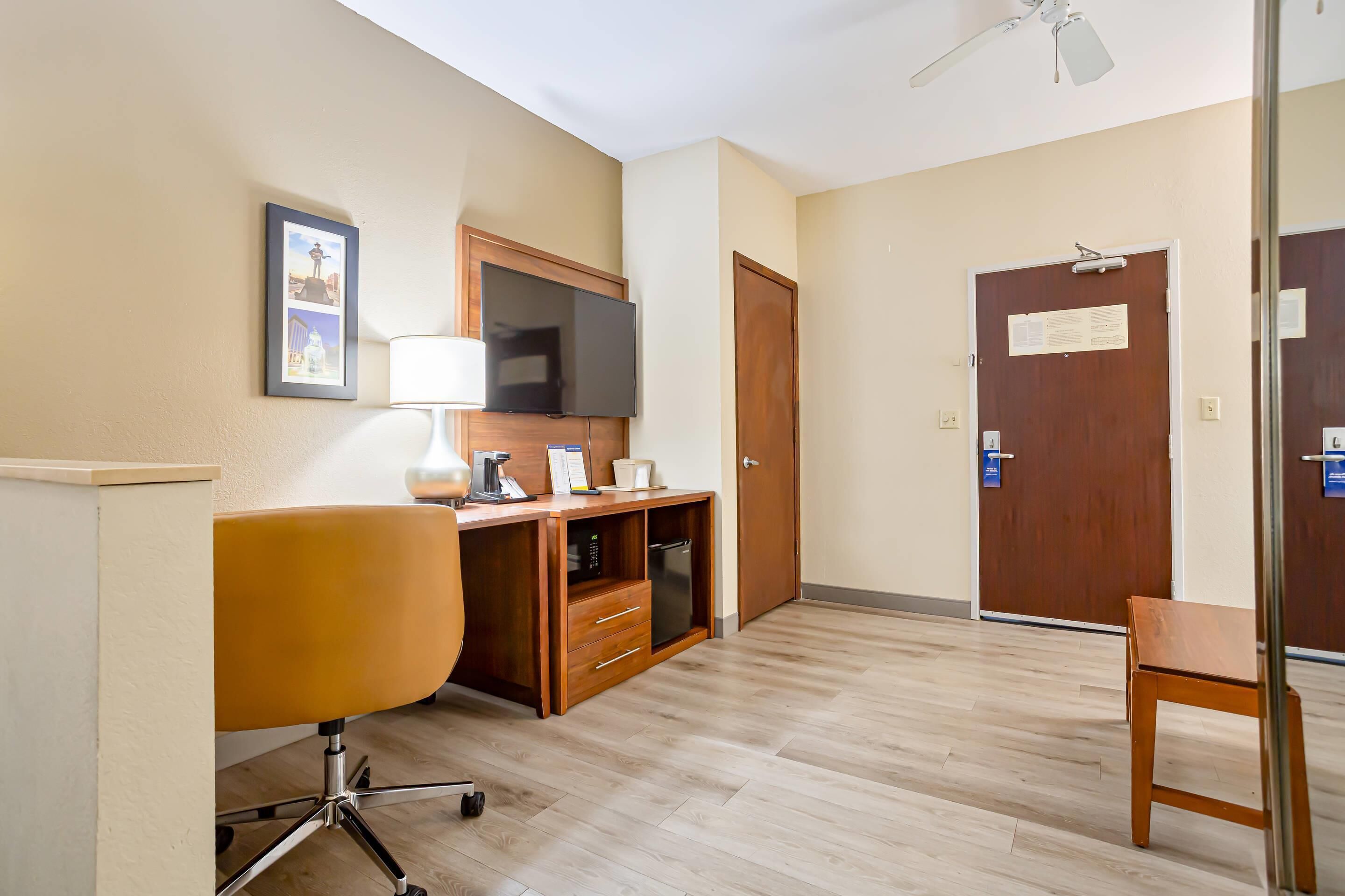 Une chambre d’hôtel avec un bureau en bois, une chaise, un téléviseur et une porte sur laquelle est affiché un avis.