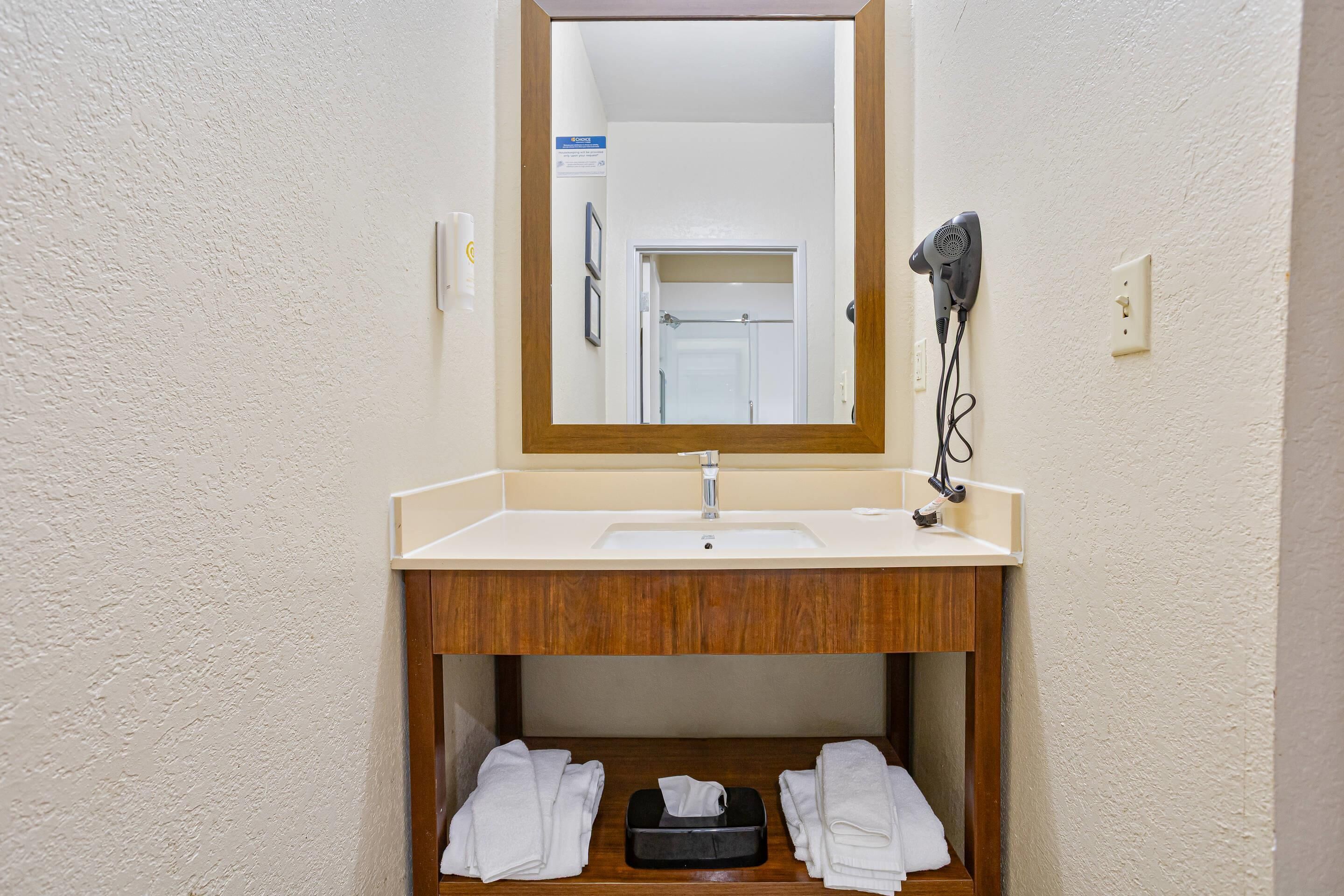 Ein Badezimmer mit einem weißen Waschbecken, einem Holz-Waschtisch, einem Spiegel und einem an der Wand montierten Föhn.