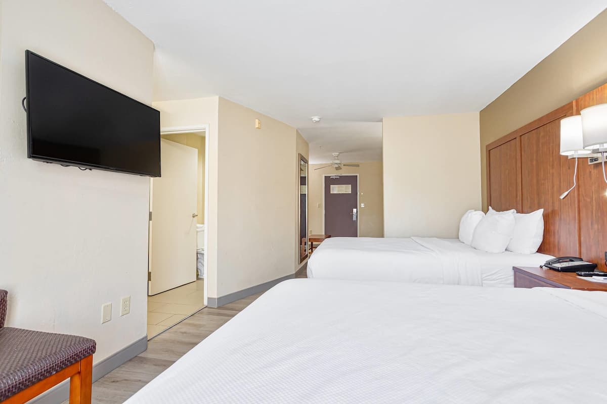 A hotel room with two beds, a flat-screen TV mounted on the wall, a wooden headboard, a bedside table, and a telephone.