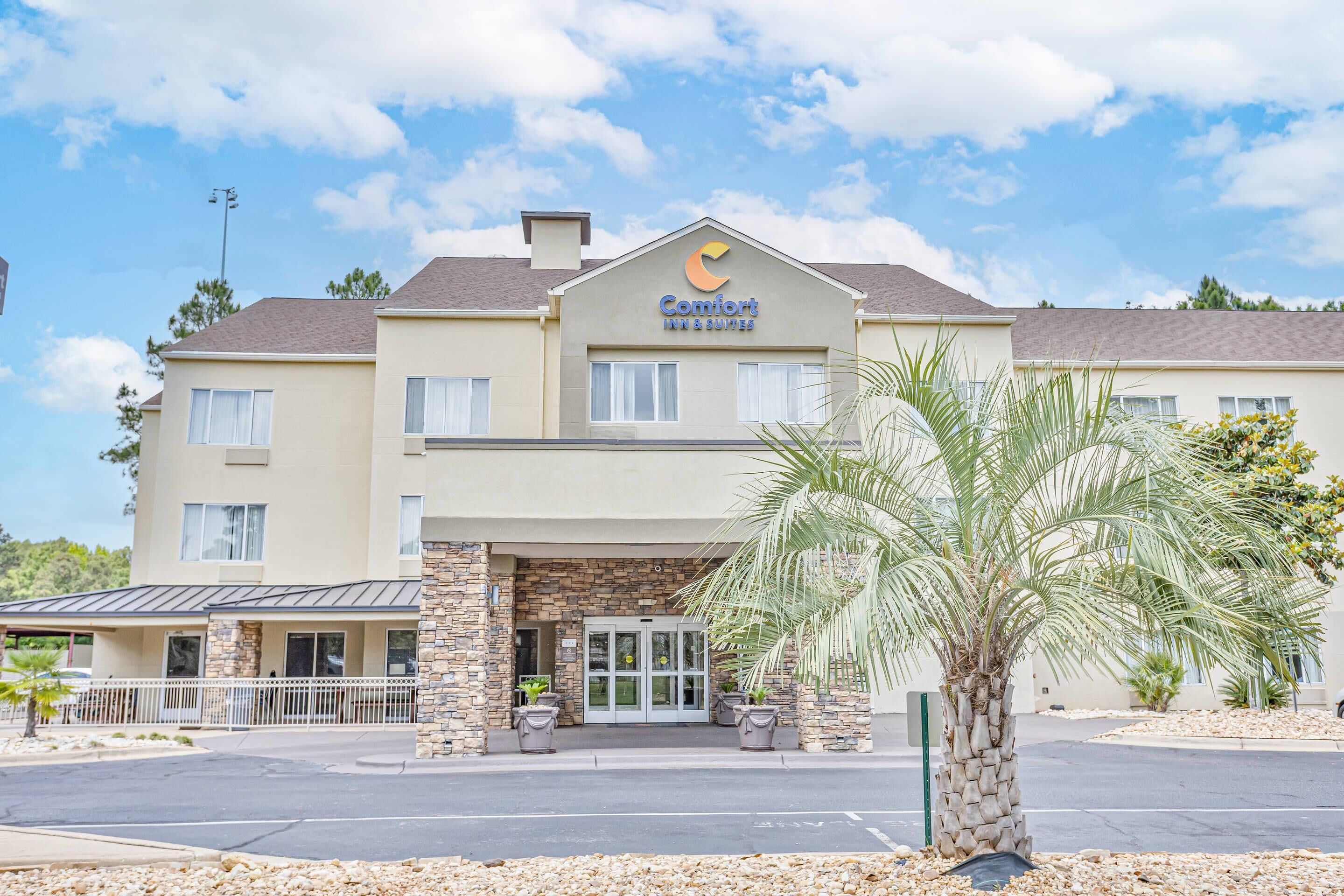 A Comfort Inn Suites hotel with a stone facade, a palm tree in the foreground, and a clear blue sky.