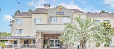 A Comfort Inn Suites hotel with a stone facade, a palm tree in the foreground, and a clear blue sky.