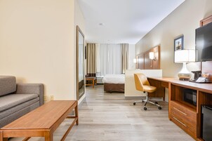 Una habitación de hotel con sofá, escritorio de madera, silla, cama, televisor y lámpara.
