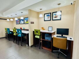 Habitación de hotel con comedor, escritorio con computadora y cuadros en la pared.