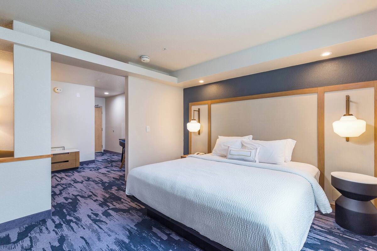 Ein Hotelzimmer mit einem großen Bett, einem Nachttisch, einer Wandlampe und einem Beistelltisch.
