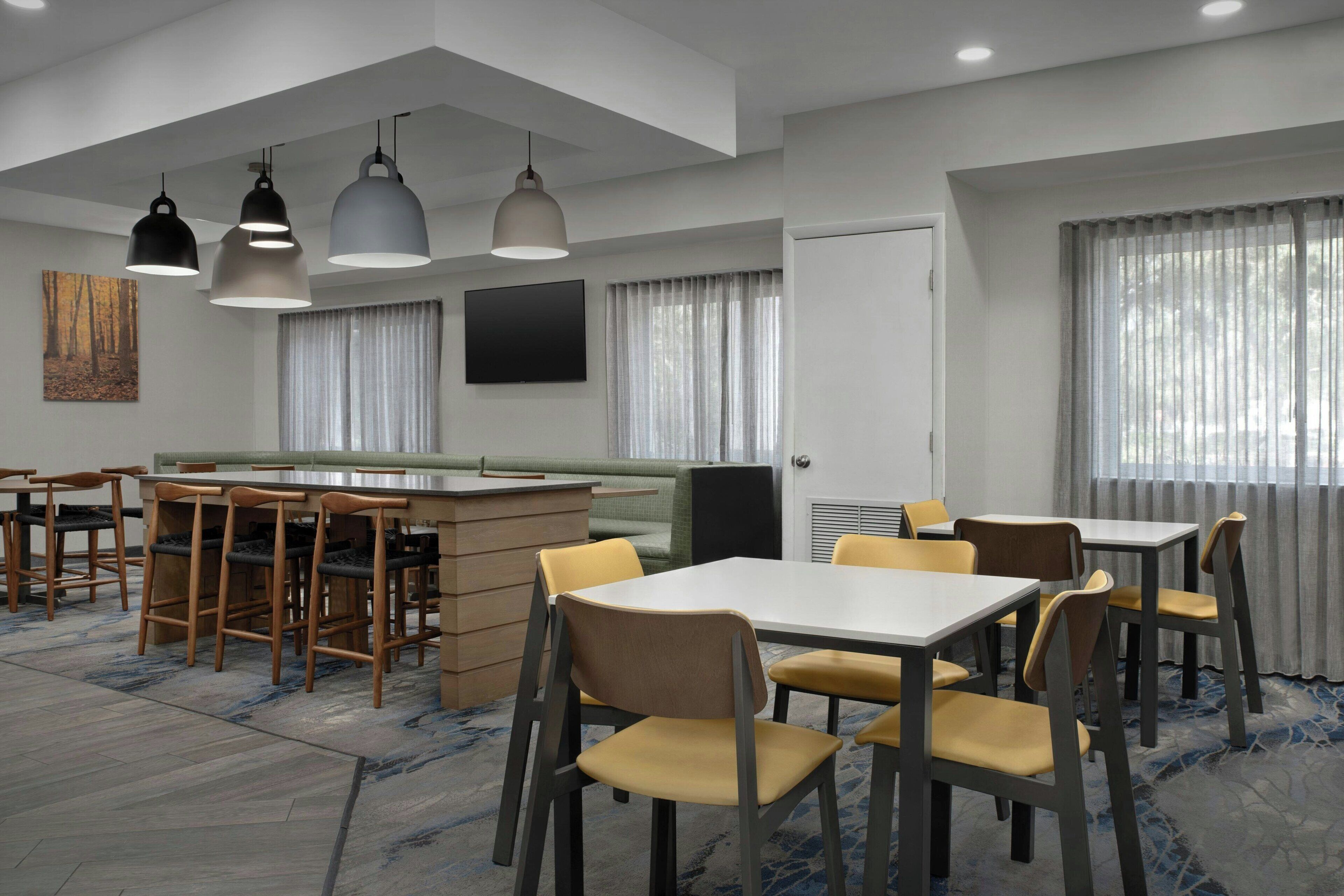 A modern dining area with multiple tables and chairs, a bar counter, and pendant lighting.