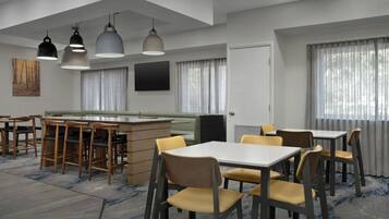 A modern dining area with multiple tables and chairs, a bar counter, and pendant lighting.