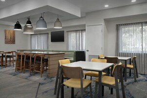 A modern dining area with multiple tables and chairs, a bar counter, and pendant lighting.