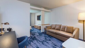 Une chambre d’hôtel avec un canapé, un bureau avec une lampe, une petite table et une vue sur le couloir.