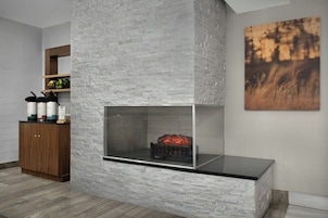 Ein modernes Interieur mit Kamin aus Steinoptik, einem Holzkabinett und einem gerahmten Kunstwerk an der Wand.