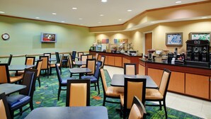 Un espace repas d’hôtel avec des tables et des chaises, un coin café et un téléviseur fixé au mur.