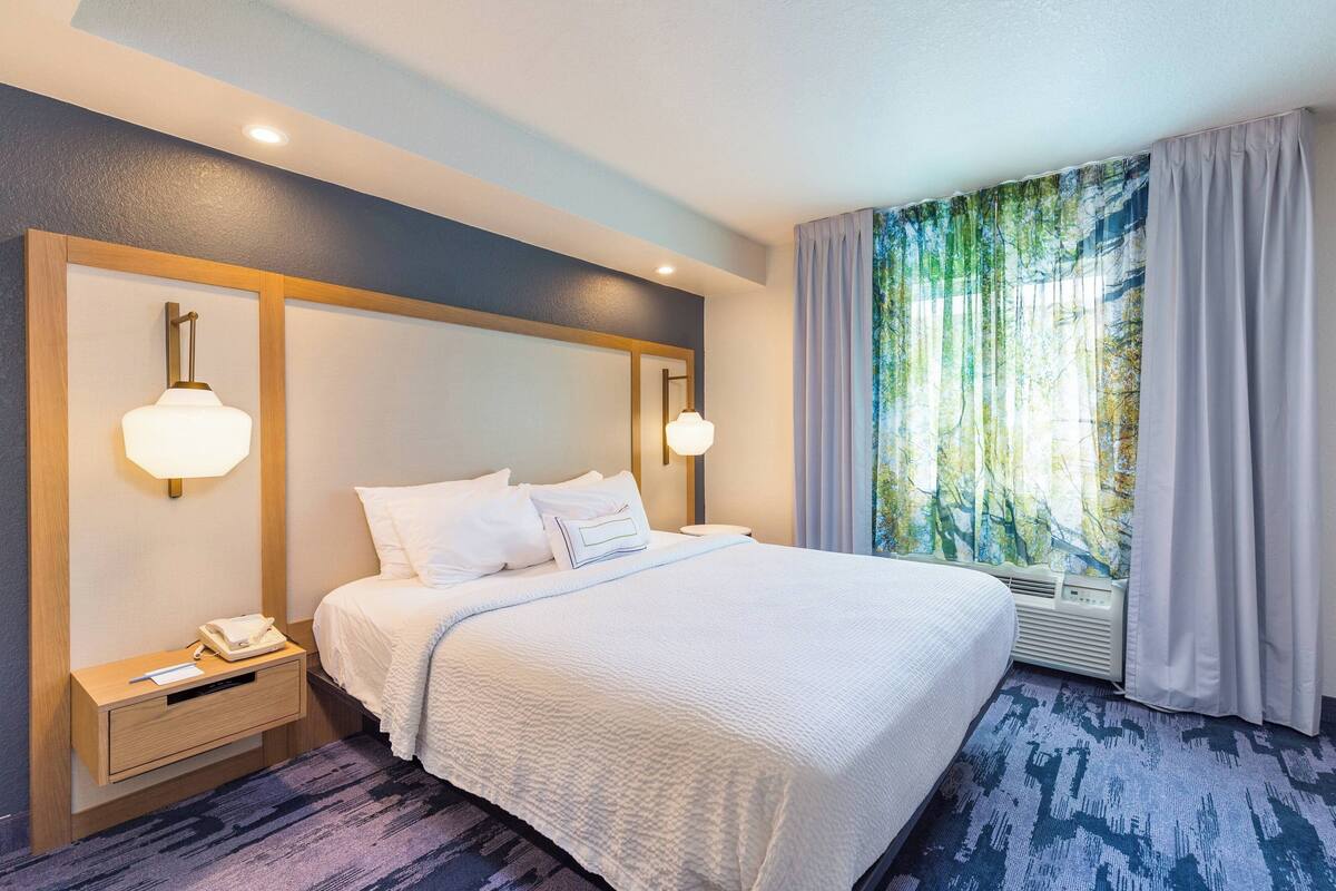 Ein Hotelzimmer mit einem großen Bett, Nachttischlampen, einem Nachttisch und einem Fenster mit Vorhängen.