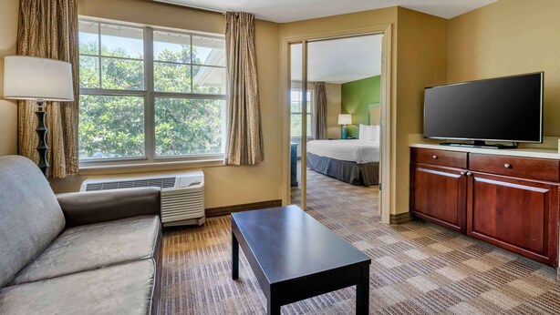 A hotel room with a sofa, a small table, a TV, a cabinet, and a large window with curtains.