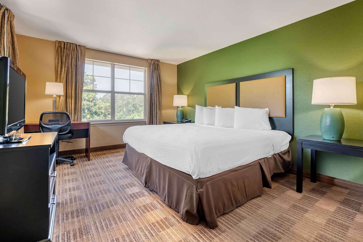 A hotel room with a large bed, a desk, two lamps, and a window with curtains.