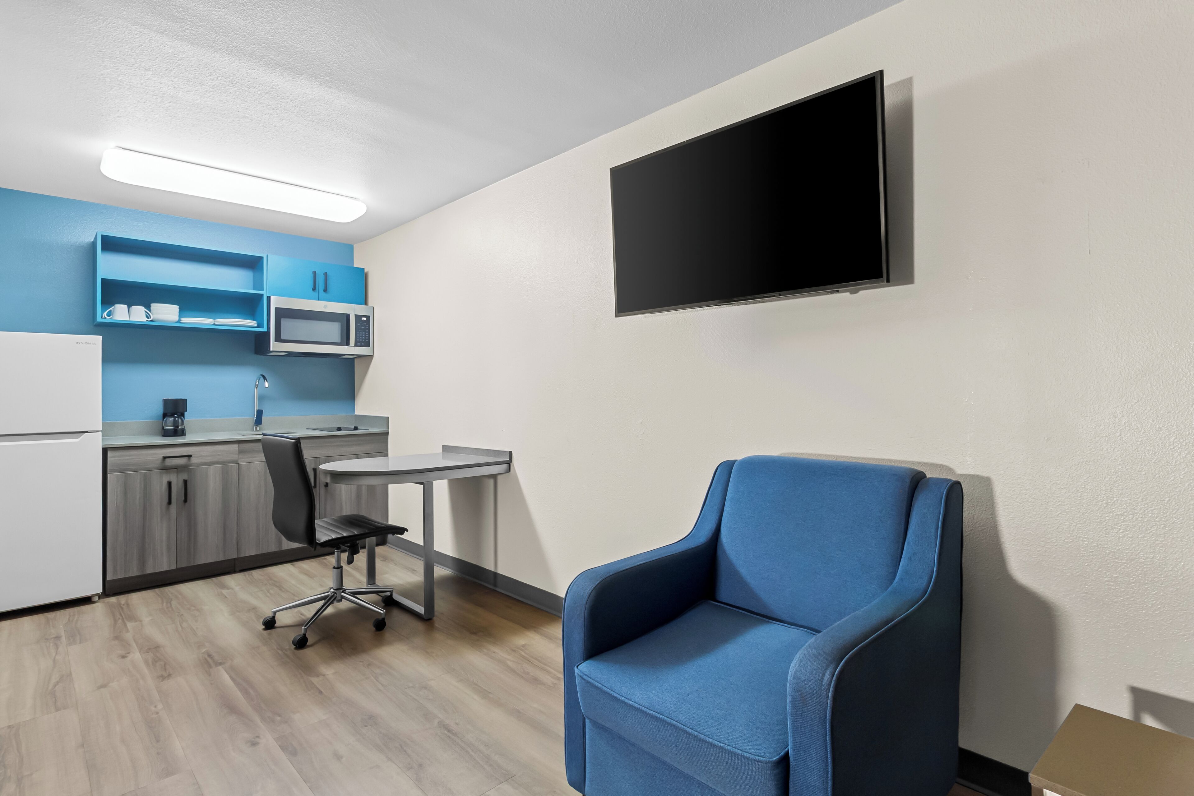 Una habitación moderna con kitchenette, televisor de pantalla plana, una silla azul y un escritorio.