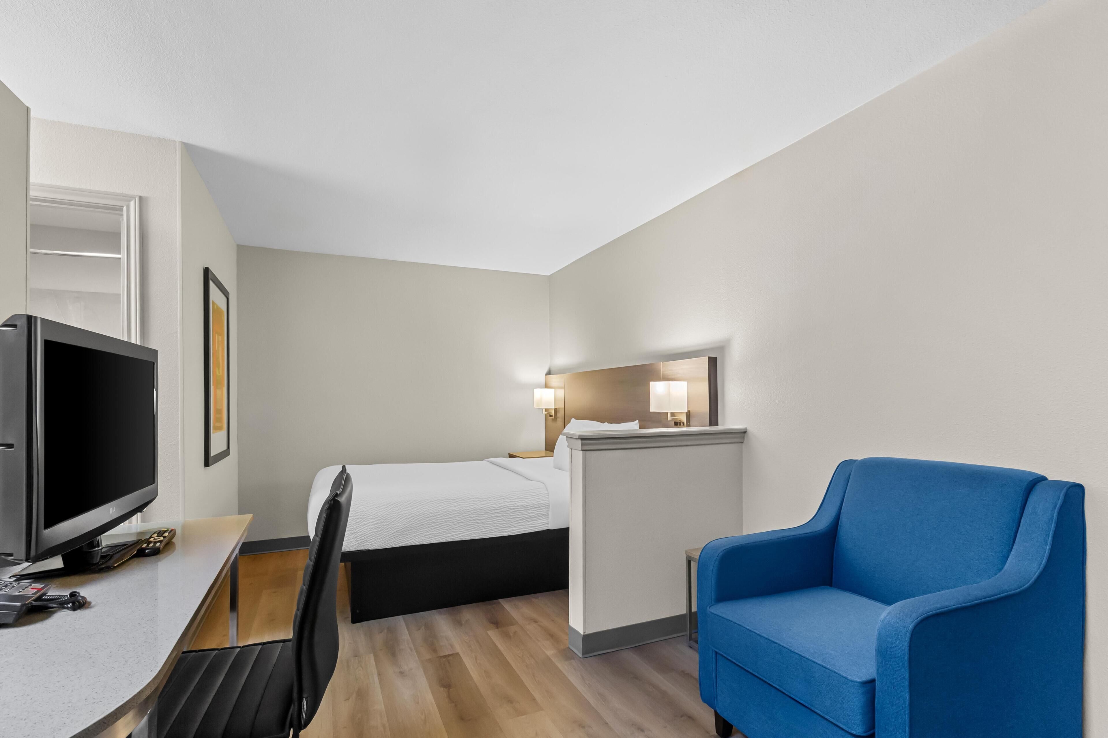 A hotel room with a bed, desk, chair, TV, and a small table.