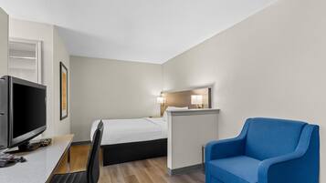A hotel room with a bed, desk, chair, TV, and a small table.