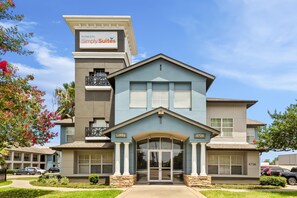 A hotel with a modern design, featuring a prominent entrance with a glass door and a sign indicating it is a Sonesta Simply Suites hotel. - Sonesta Simply Suites Stafford (Stafford)