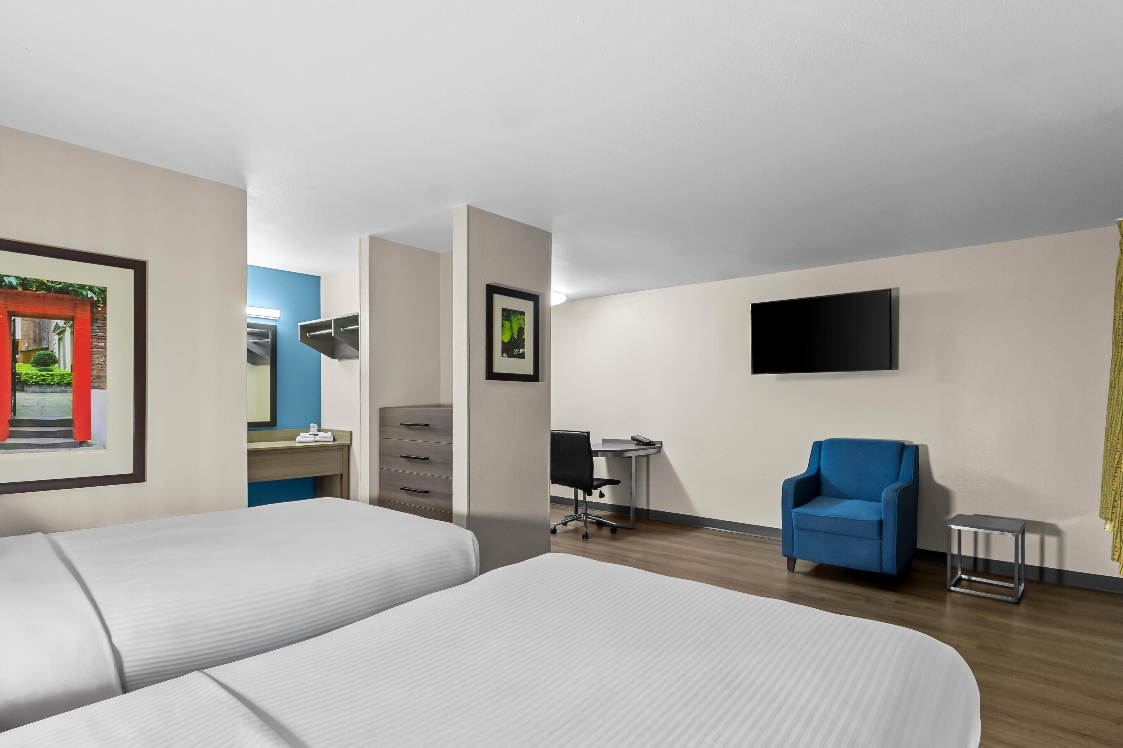 A hotel room with two beds, a desk, a chair, a TV, and a framed picture on the wall.