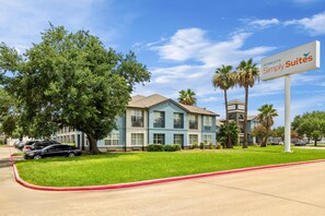 A hotel with a sign for 'Sonesta Simply Suites' featuring a two-story building with balconies, surrounded by greenery and palm trees. - Sonesta Simply Suites Stafford (Stafford)