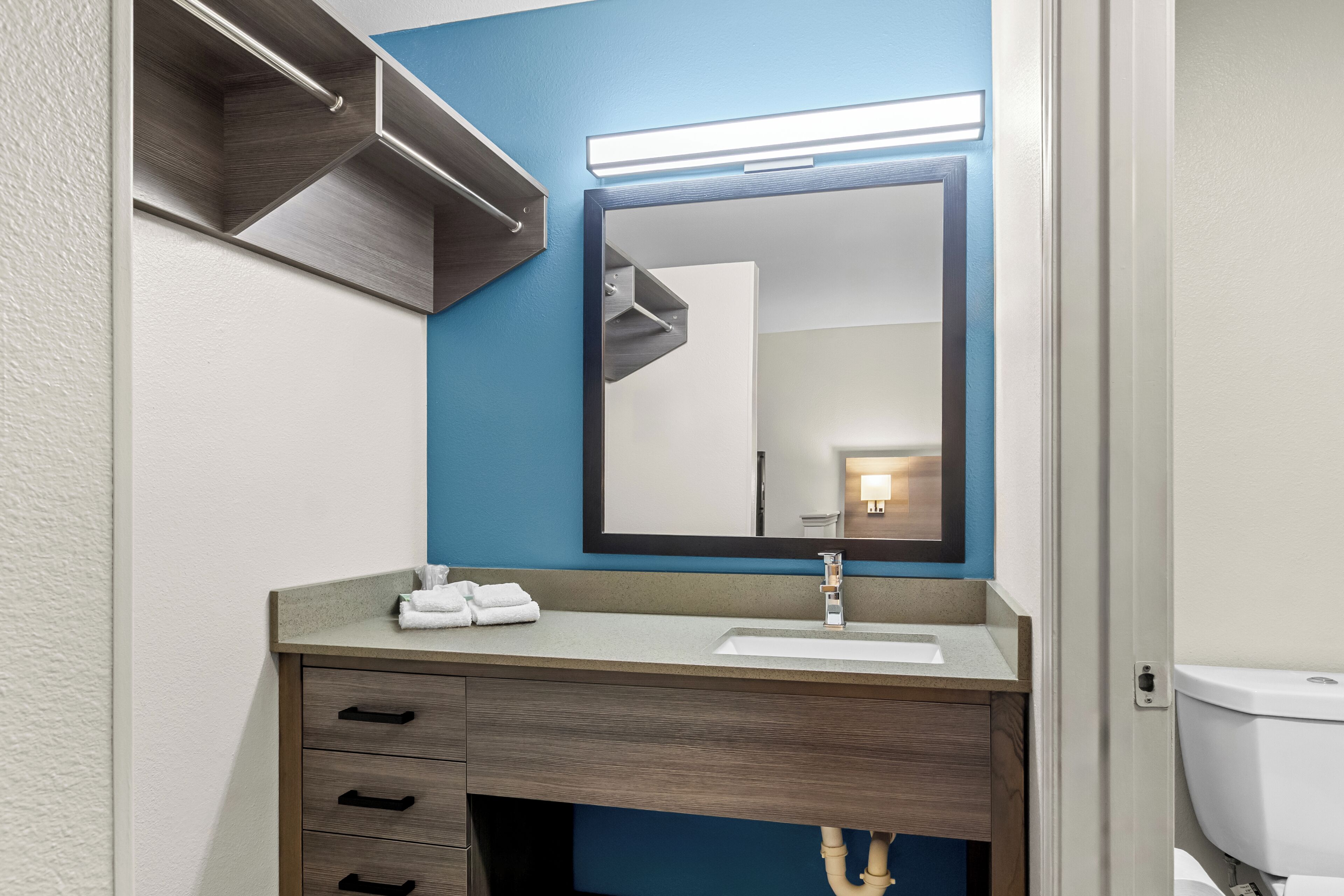 Un baño con lavamanos, espejo, toallero y tocador de madera.