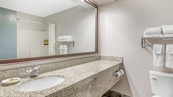 Un baño con lavamanos de encimera de granito, un espejo grande y un toallero con toallas dobladas.