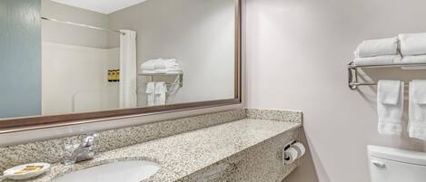 A bathroom with a granite countertop sink, a large mirror, and a towel rack with folded towels.