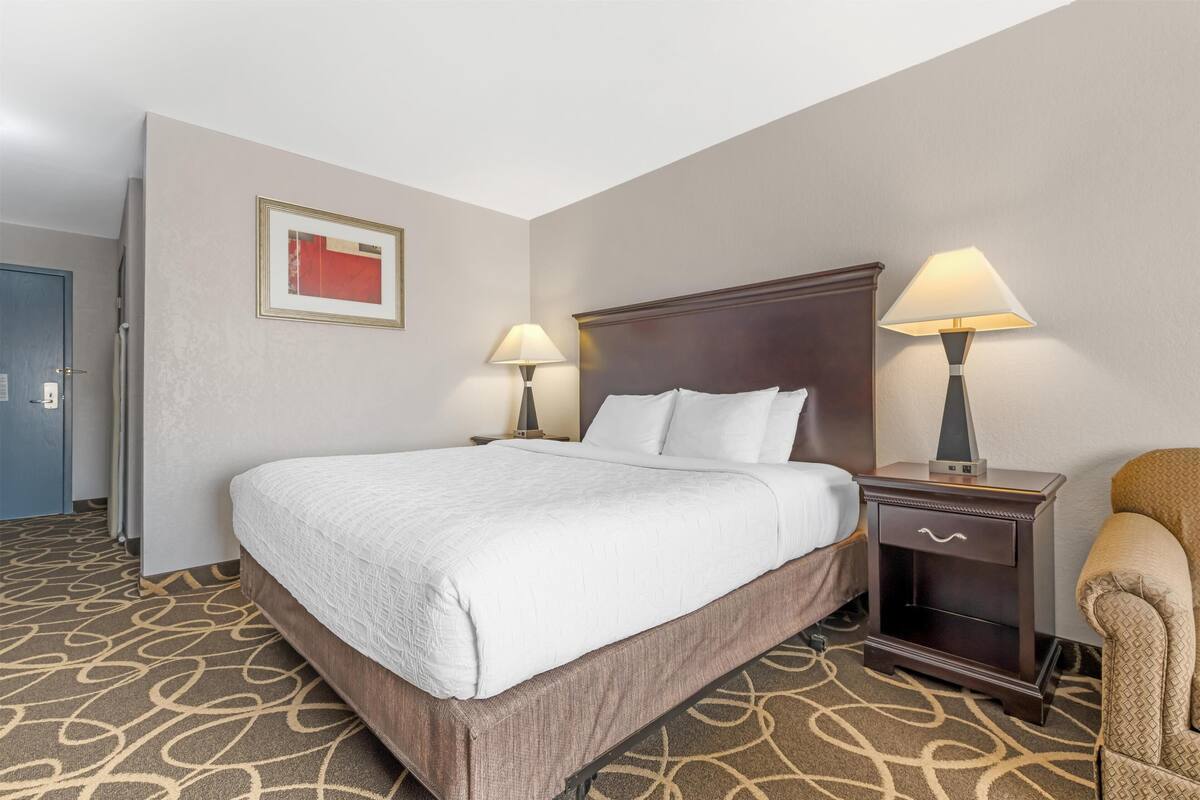 Una habitación de hotel con una cama grande, dos mesitas de noche con lámparas, una silla y una puerta.