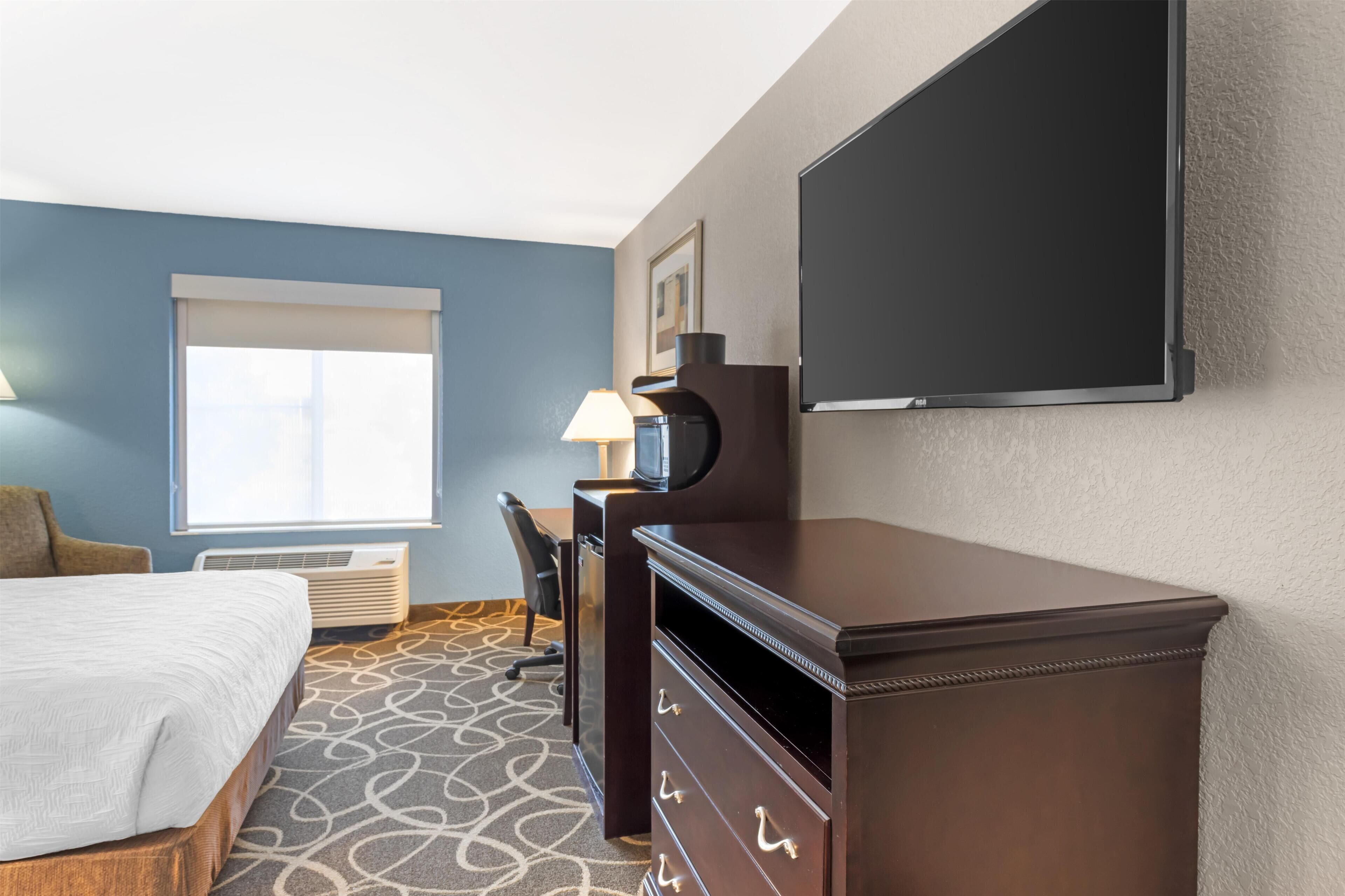 A hotel room with a bed, desk, chair, TV, and a large window.