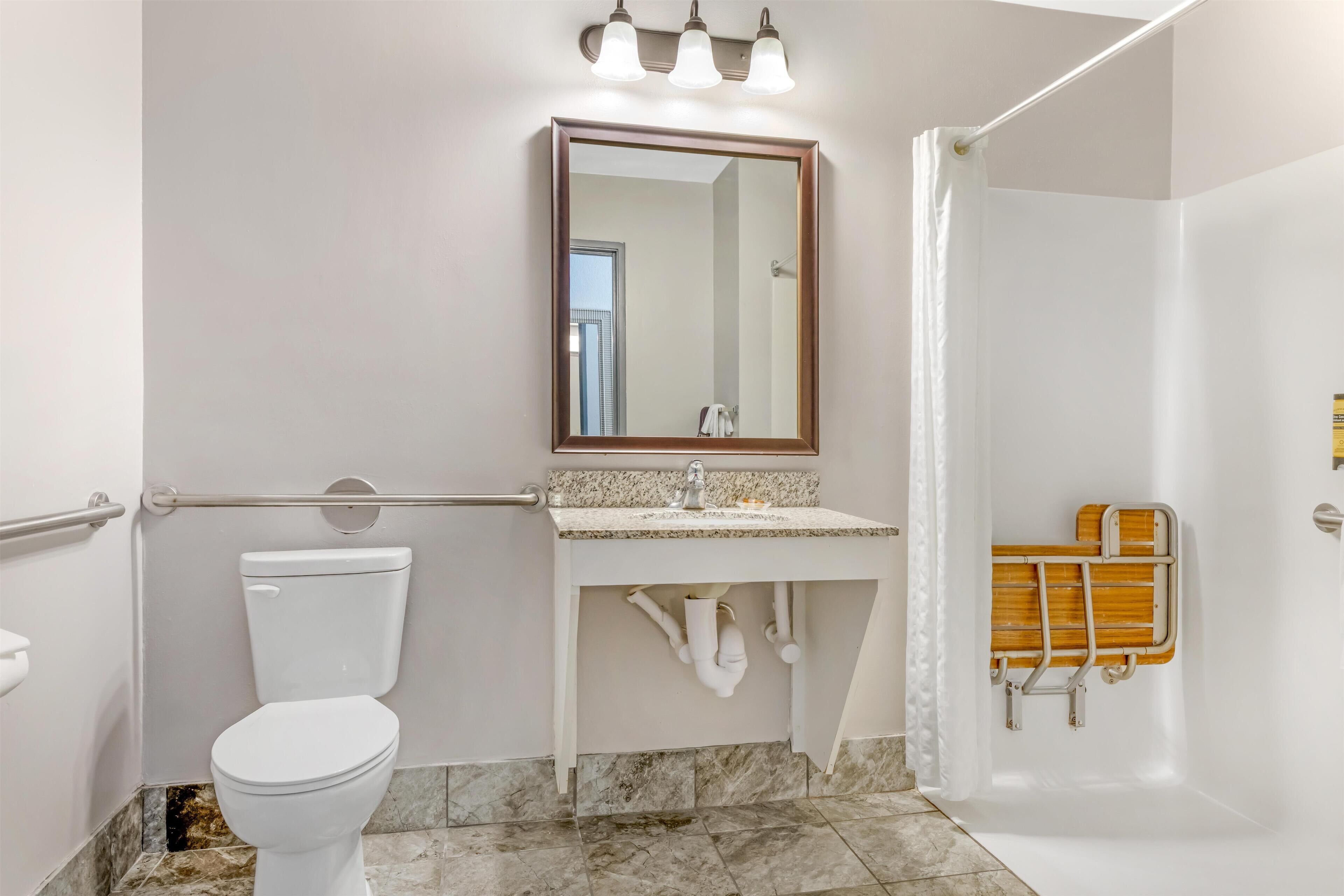 A bathroom with a toilet, sink, mirror, and shower area.