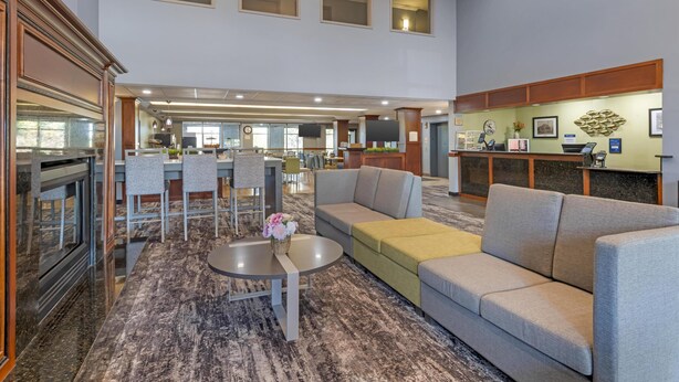 A spacious lobby with a grey sofa, a round table with a vase, and a reception desk. - Best Western Plus Eau Claire Conference Center (Eau Claire)