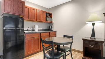 Una cocina compacta con armarios de madera, un refrigerador negro, un microondas, una mesa con sillas y una lámpara.