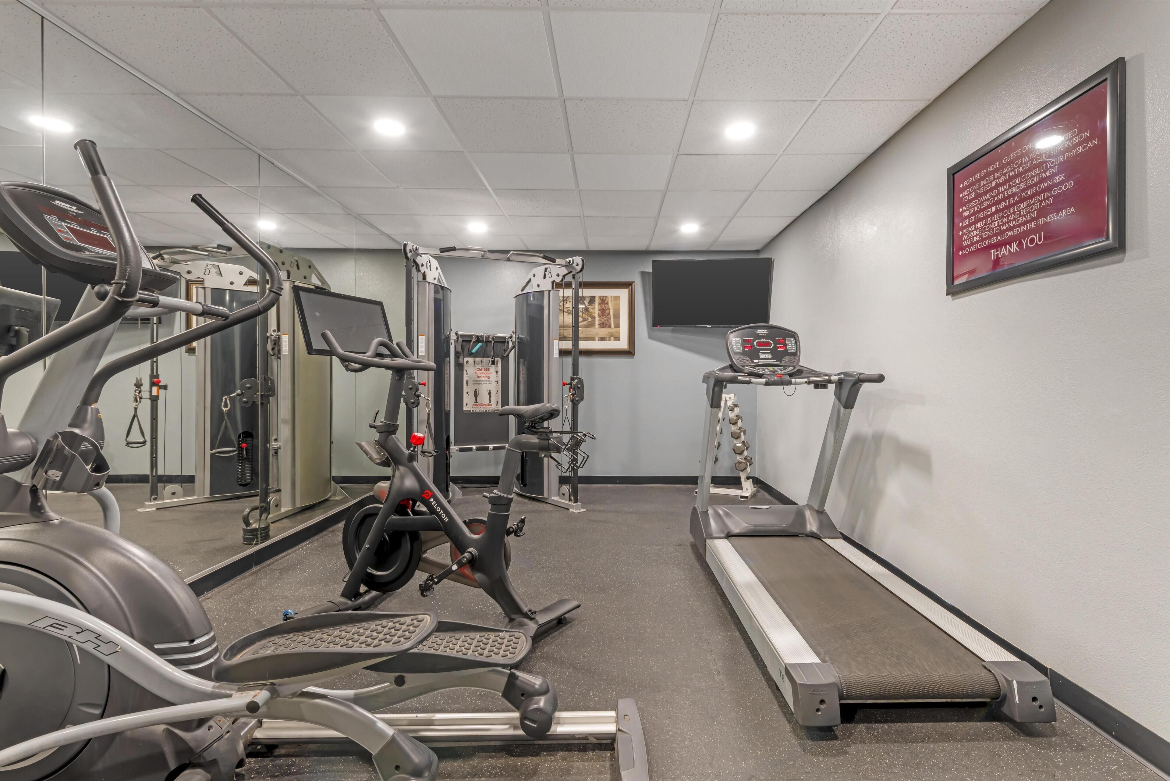 Un gimnasio con máquinas de cardio, equipo de entrenamiento con pesas y una cinta de correr.