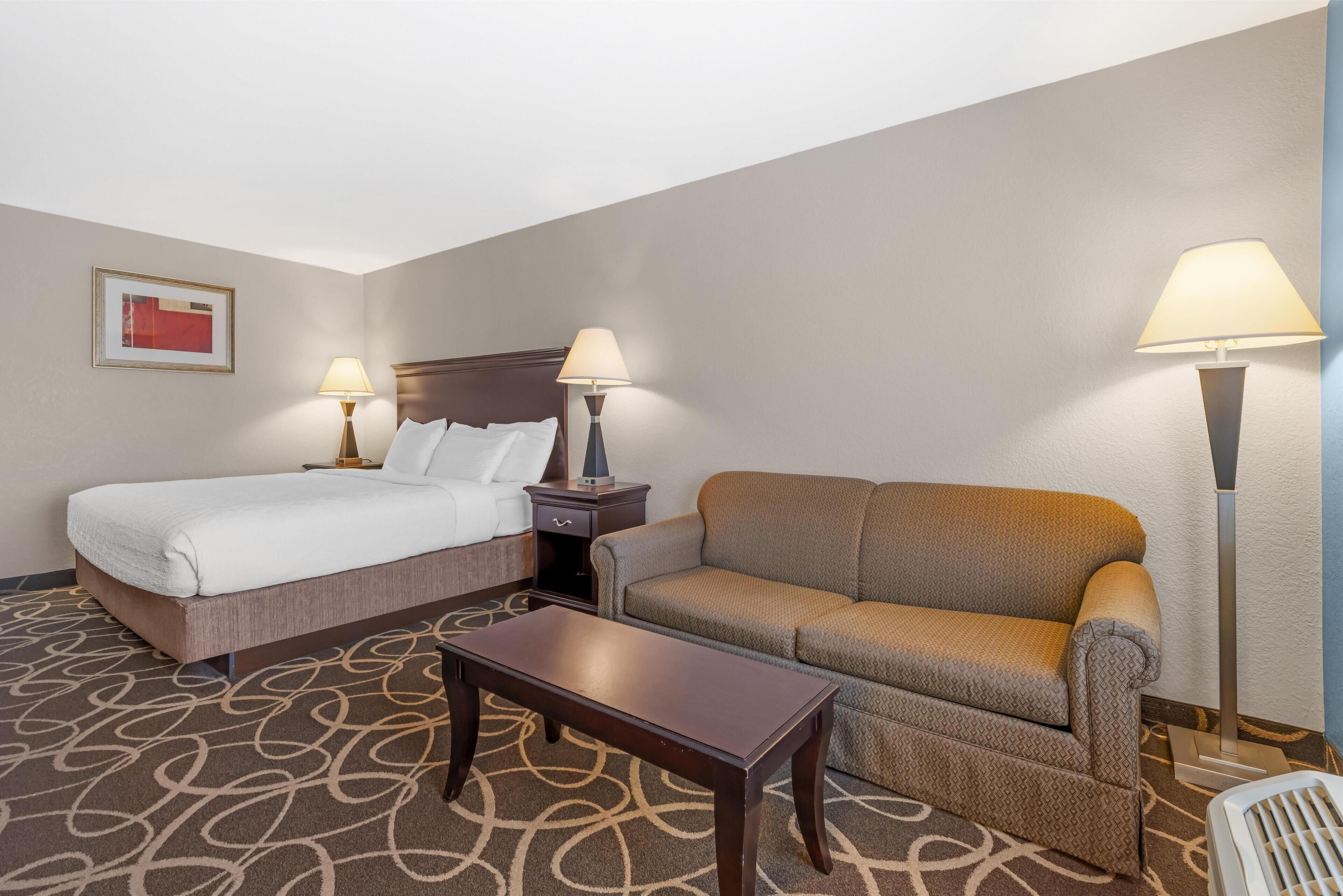 Una habitación de hotel con una cama, un sofá, una mesa, dos lámparas y una silla.